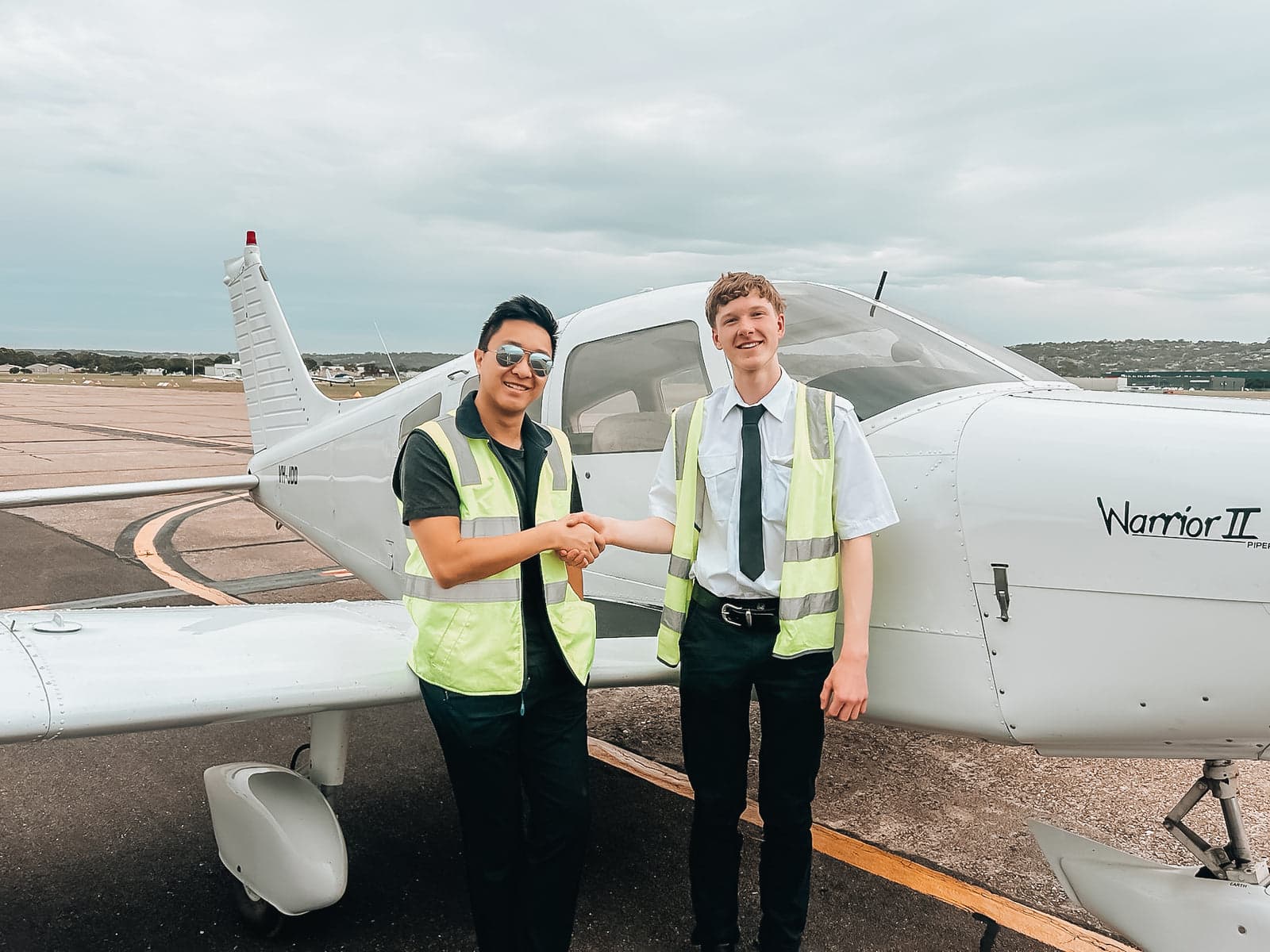 An instructor congratulates a student pilot beside a Piper Warrior II on the apron
